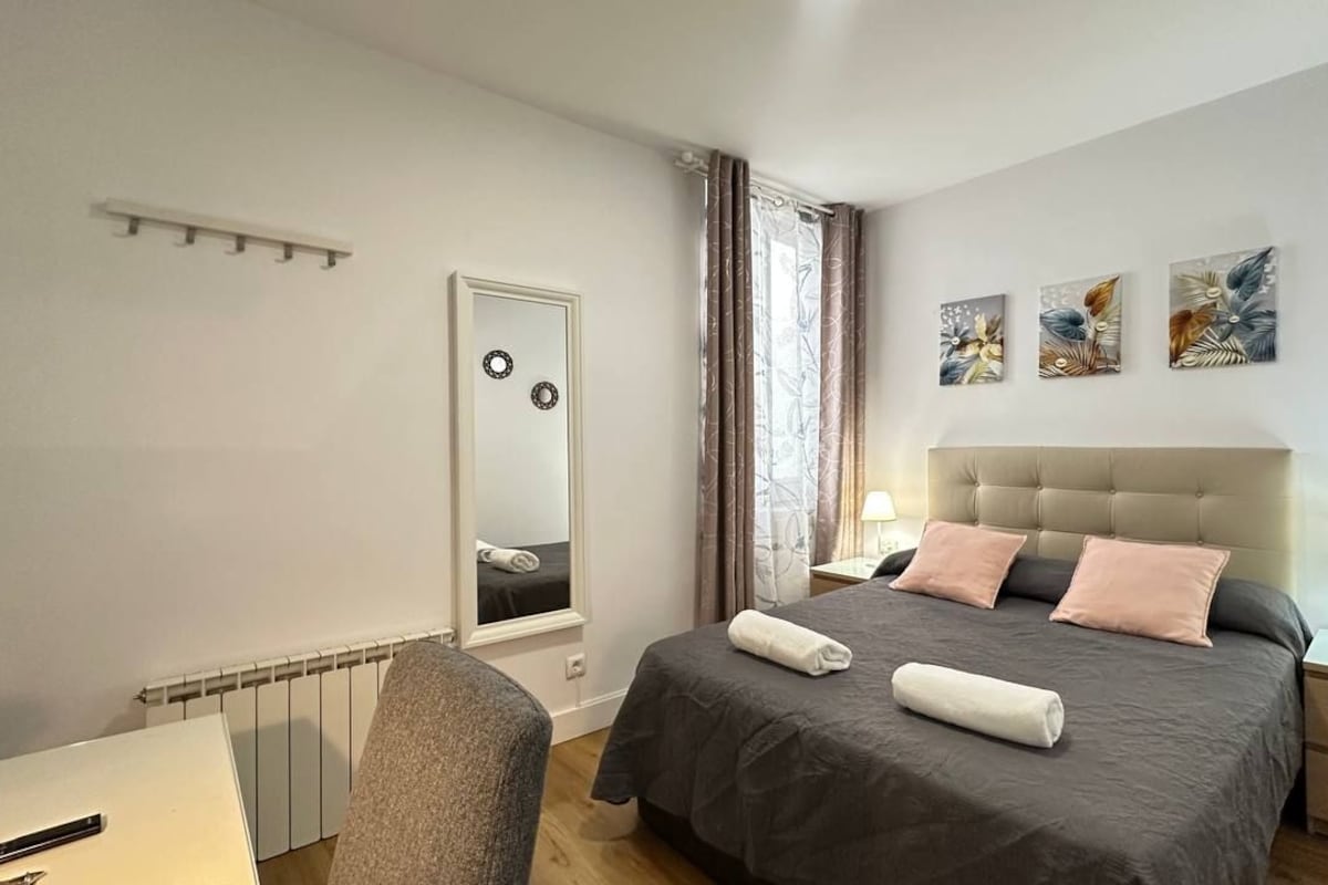 Un dormitorio con cama, mesitas de noche, un espejo y obras de arte en la pared.