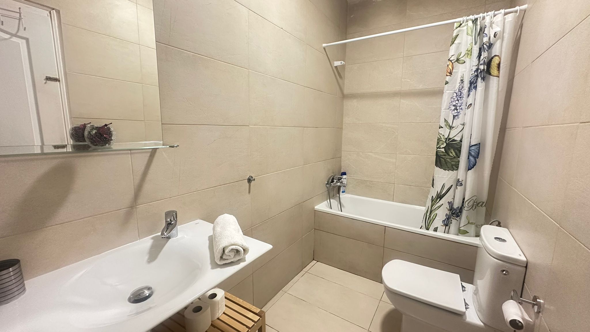 A bathroom with a white sink, toilet, and shower. There is a towel on the sink and a shelf above it.