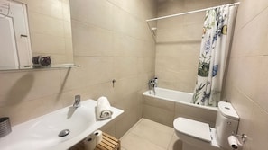 A bathroom with a white sink, toilet, and shower. There is a towel on the sink and a shelf above it.