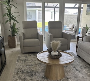 A living room with two beige armchairs, a round wooden coffee table, and a potted plant. - NEW 3BR Pool Home on Woodlands 10th Green, Walk to Eastport, 4 Seater Golf Cart (The Villages)