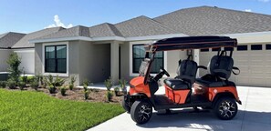 Carrinho de golfe estacionado em frente a uma casa moderna com garagem.