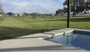 A swimming pool with a clear view of a residential area in the background. - NEW 3BR Pool Home on Woodlands 10th Green, Walk to Eastport, 4 Seater Golf Cart (The Villages)