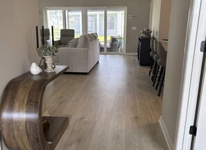Un salon moderne avec une console en bois aux lignes courbes, un canapé gris et un coin repas agrémenté de tabourets de bar.