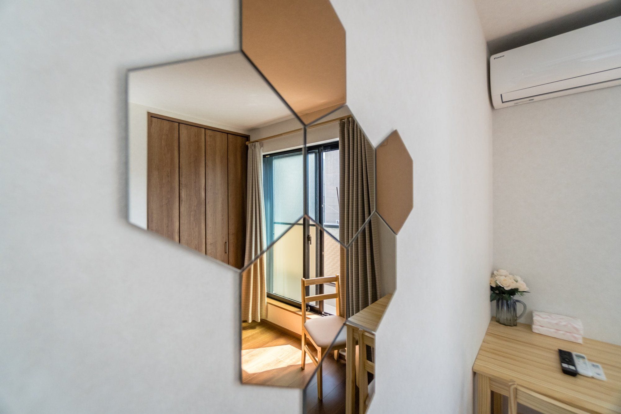 A modern interior with a geometric wall design, a wooden wardrobe, a chair, and a small table with a vase and remote controls.