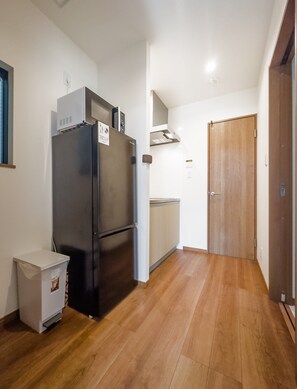 A compact kitchen with a black refrigerator, a small trash bin, and a wooden door. - HANASTAY URA (Osaka)