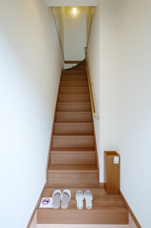 A wooden staircase with a handrail, leading to a landing with a shoe rack and a sign. - HANASTAY URA (Osaka)