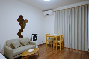 A living room with a sofa, a small table, a fan, and a window with curtains. - HANASTAY URA (Osaka)