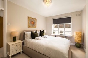 A neatly made bed with white linens, a bedside lamp, a decorative wall piece, and a window with a view. - 10 Mins Walk to Selfridges Marylebone Retreat (London)