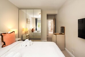 A hotel room with a bed, a bedside table, a mirror, a TV, and a view into the hallway. - 10 Mins Walk to Selfridges Marylebone Retreat (London)