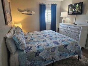 Ein Schlafzimmer mit einem Bett, einer Kommode, einer Lampe, einer Wanddekoration in Fischform und einem Fernseher.