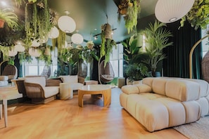A modern living room with a sofa, chairs, hanging plants, and a large window. - Luxury 2BR Apt| Water & Skyline Views | 29th Floor (Miami)