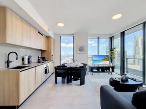 A modern kitchen with a dining area, large windows with a city view, and a flat-screen TV. - Luxury 2BR Apt| Water & Skyline Views | 29th Floor (Miami)