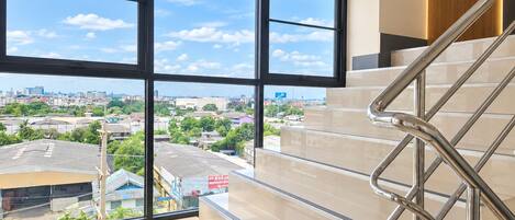 A modern hotel interior with a staircase leading to a balcony, offering a city view.