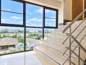 A modern hotel interior with a staircase leading to a balcony, offering a city view. - OK Residence Minburi (Bangkok)