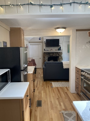Cocina compacta con microondas, refrigerador y estufa. También se ve una chimenea de piedra y un televisor de pantalla plana.