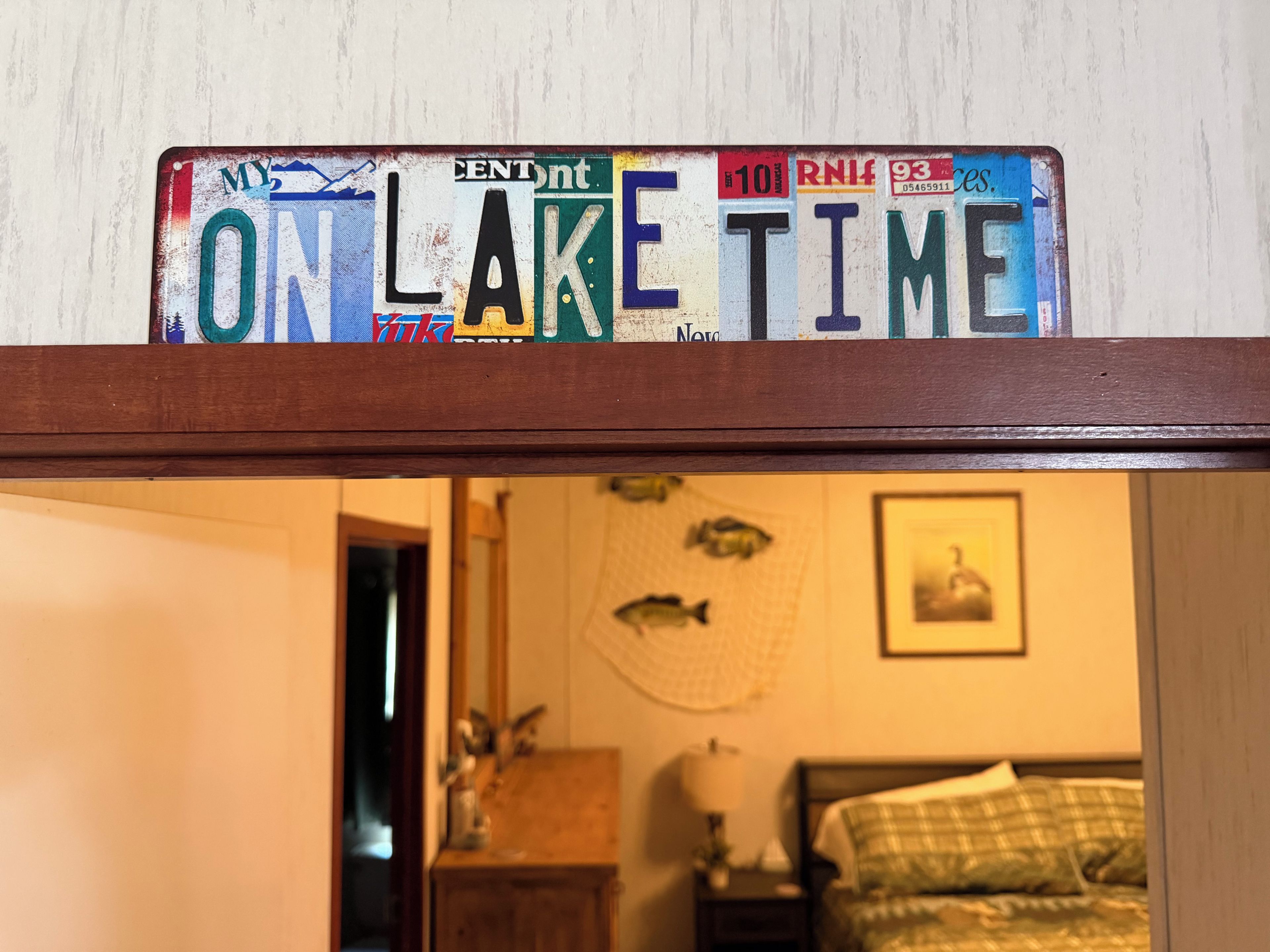 Eine Wand mit einem Nummernschild, das 'ONLAKE TIME' zeigt, und ein Zimmer mit einem Bett, einem Nachttisch und einer Wanddekoration.