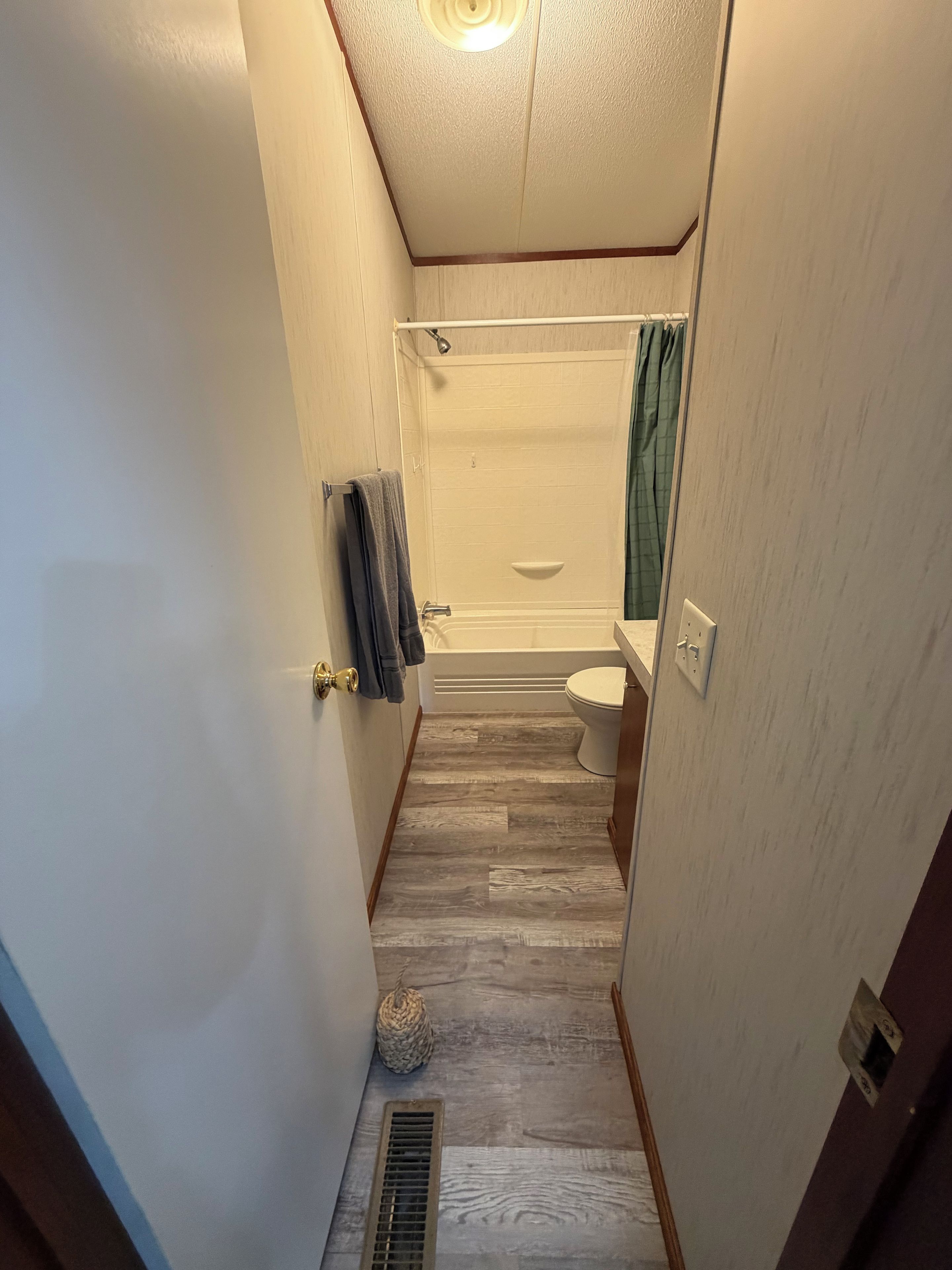 A narrow bathroom with a shower, toilet, and a towel rack.