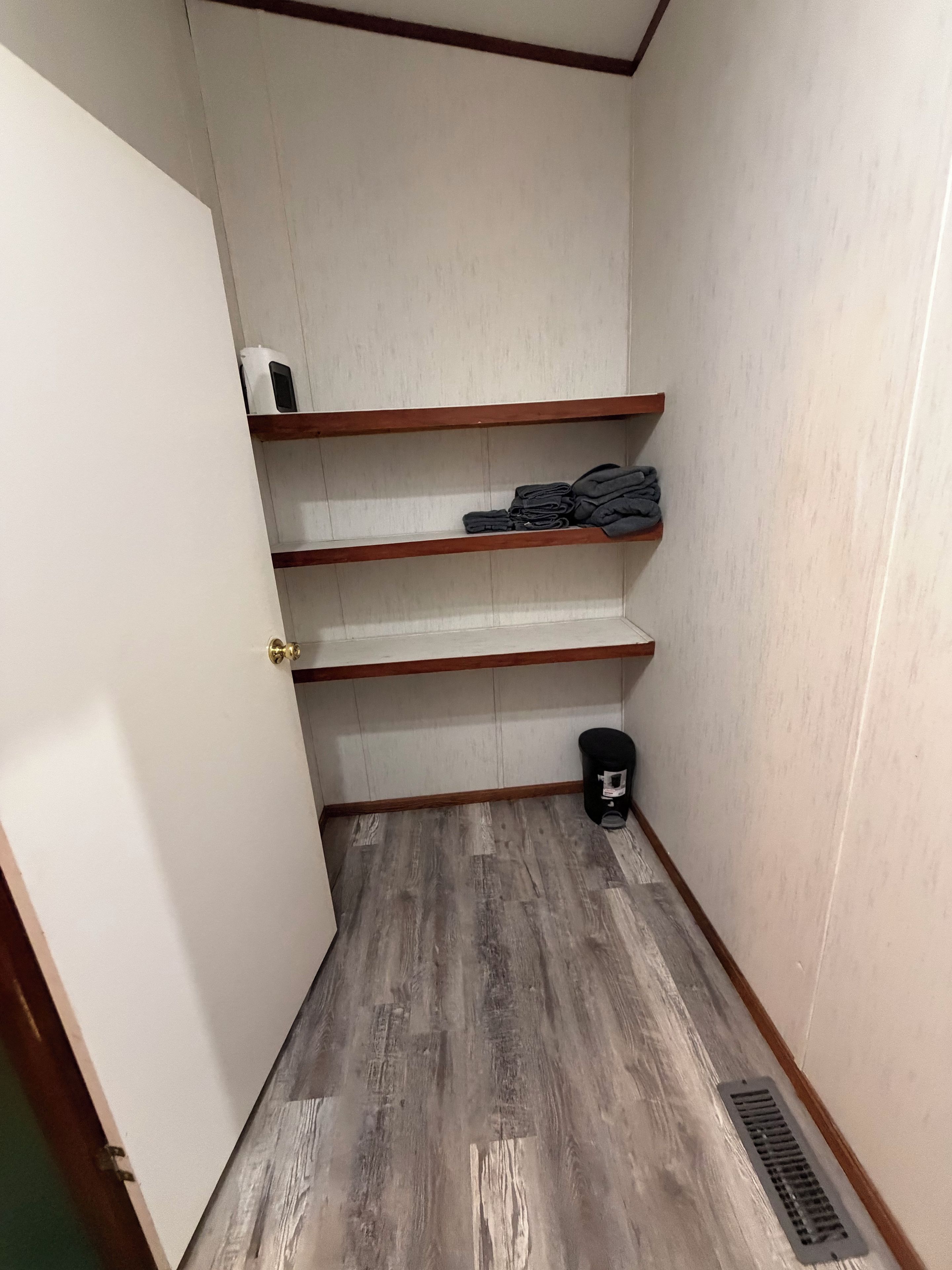 Una habitación pequeña con piso de madera, una puerta y un estante con ropa doblada.