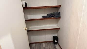 Una habitación pequeña con piso de madera, una puerta y un estante con ropa doblada.