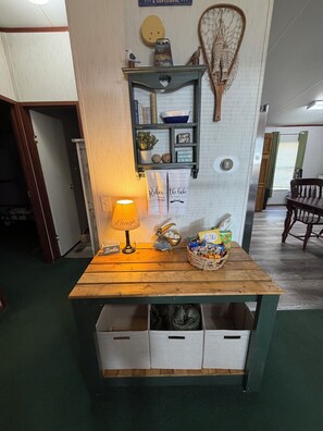 A wooden table with a lamp, a basket of snacks, and a wall-mounted shelf with decorative items.