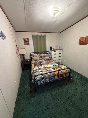 A bedroom with a bed, a dresser, a lamp, and a green carpet.