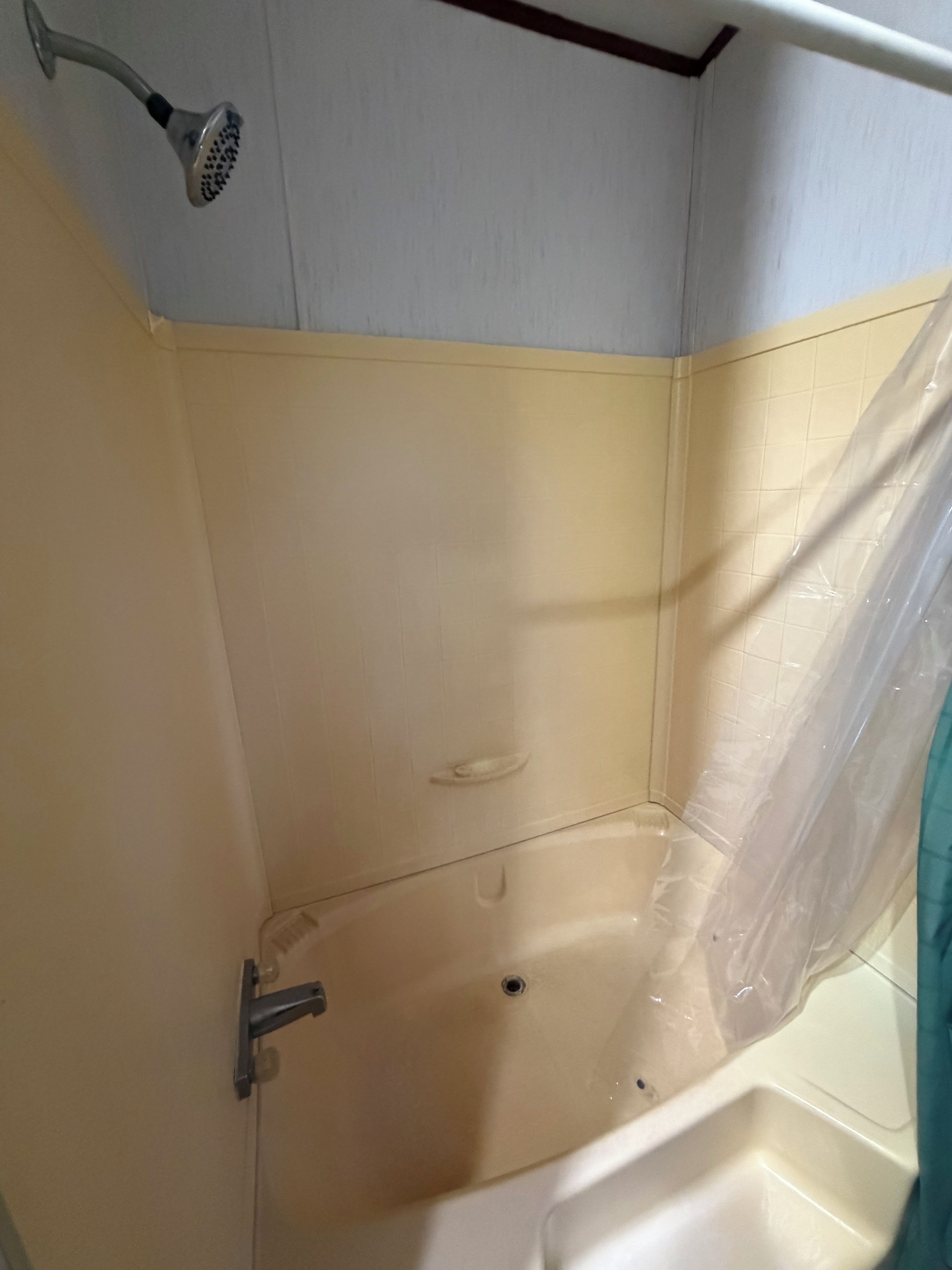 A shower area with a showerhead, a drain, and a plastic curtain.