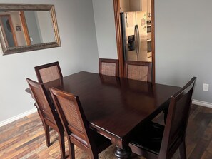 Comedor con una mesa rectangular, seis sillas de madera con asientos de rejilla, piso de madera y un espejo fijado a la pared.