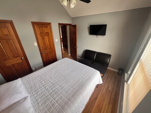 Un dormitorio con una cama, un sofá de cuero negro, un televisor en la pared y puertas de madera.