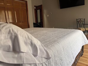 Un dormitorio con una cama, un armario de madera, un televisor montado en la pared y una silla.