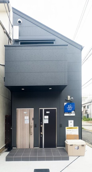 A building with two doors, a blue sign, and a cardboard box on the sidewalk. - HANASTAY TAKE (Osaka)
