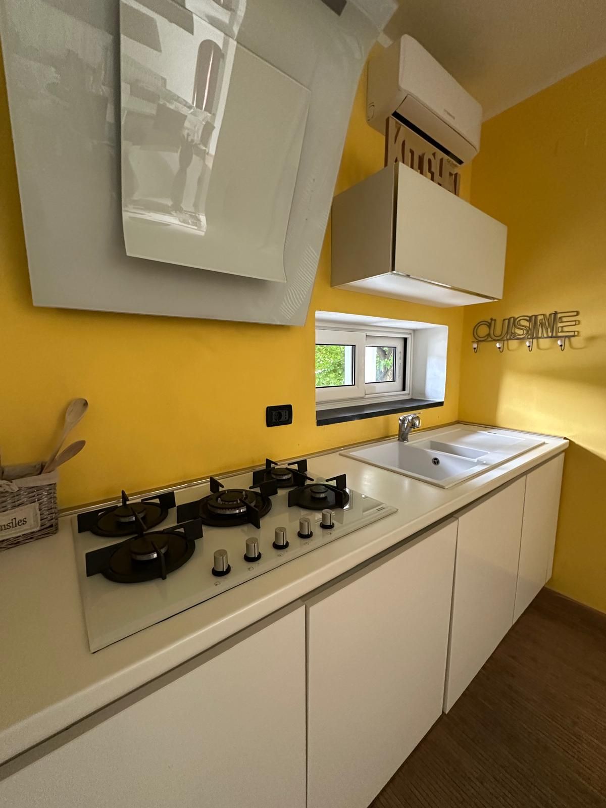 Une cuisine moderne équipée d’une cuisinière à gaz, d’un four encastré, d’un plan de travail blanc et d’un mur jaune.