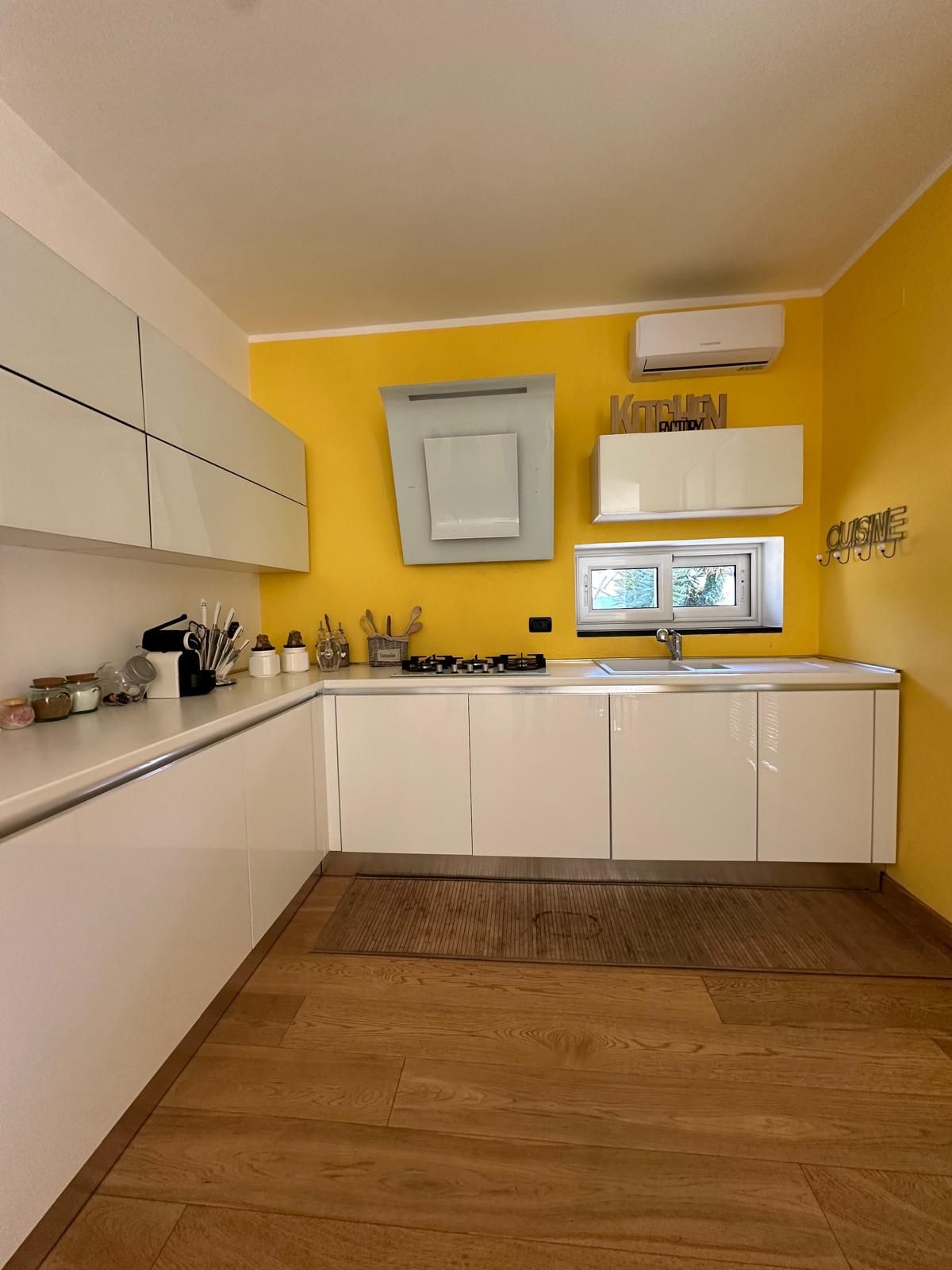 A modern kitchen with white cabinets, a yellow wall, and a wooden floor.
