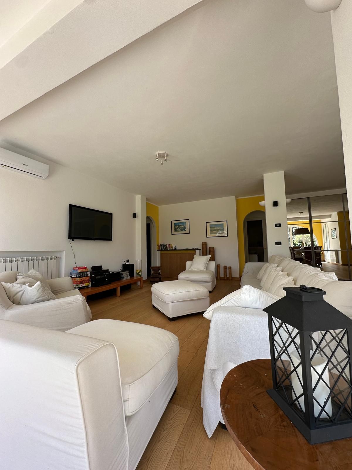 A spacious living room with a large sofa set, a coffee table, and a TV mounted on the wall.
