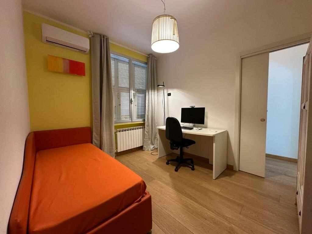 Una habitación con cama, escritorio, silla, aire acondicionado, ventana con persianas y puerta.