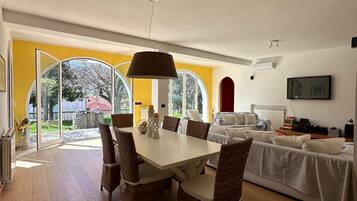 Ein geräumiger Wohnbereich mit Esstisch und Stühlen, einer Couch und einem an der Wand befestigten Fernseher.