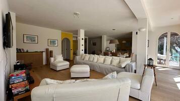 A spacious living room with a large sofa, a coffee table, and a television mounted on the wall.
