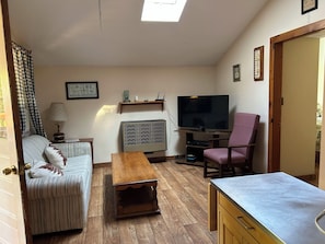Ein Wohnzimmer mit einer Couch, einem Fernseher, einem Couchtisch, einem Sessel und einem Schrank.