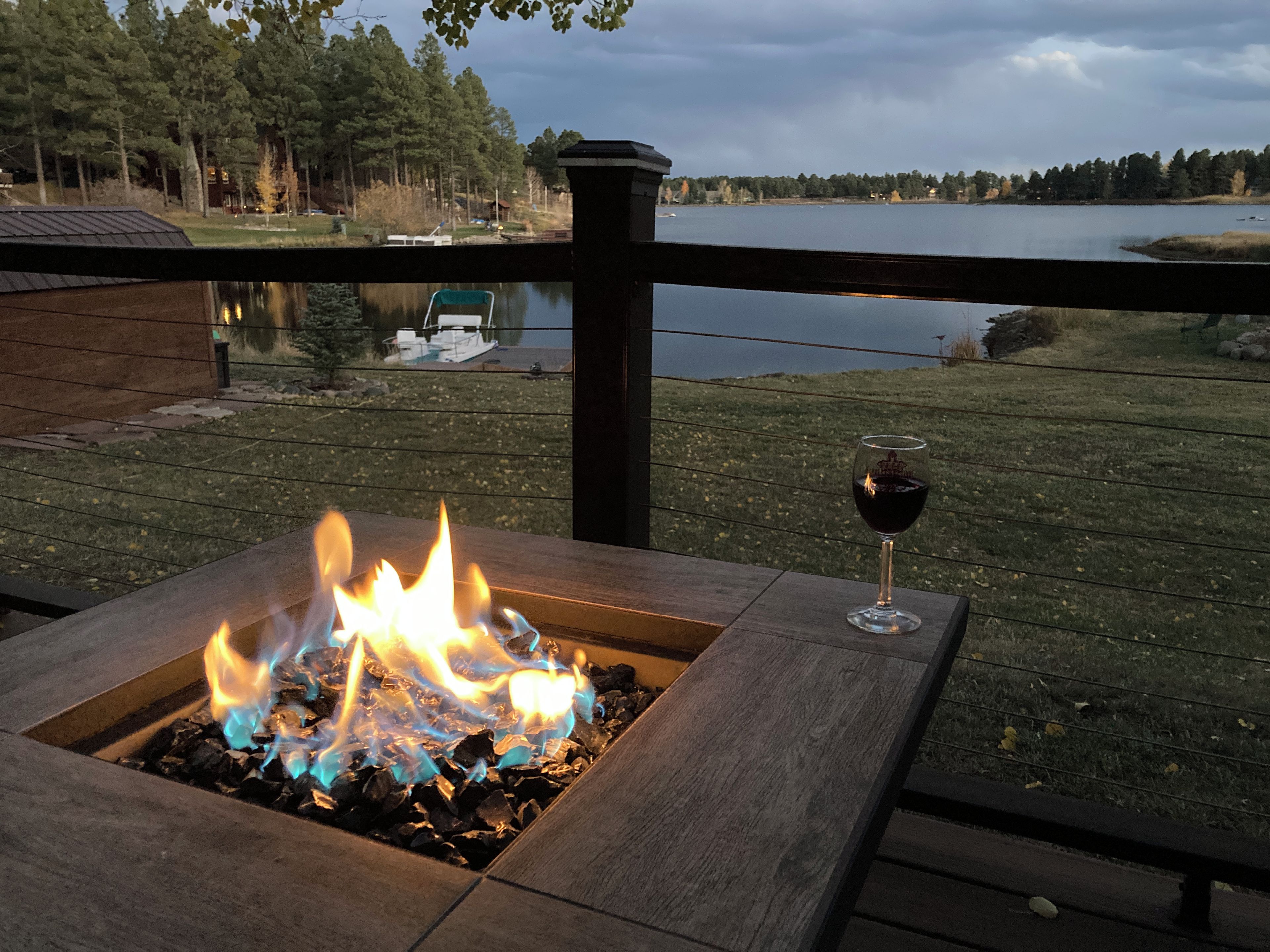 Un foyer extérieur, accompagné d'un verre de vin rouge, sur une terrasse donnant sur un lac.