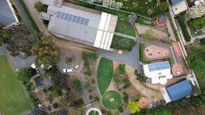 An aerial view of a residential area with solar panels, a tennis court, and a landscaped garden. - New one of two 2-bedroom units in Gawler-Barossa. Unique garden. Close to shops (Evanston)