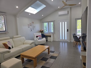 A modern living room with a sofa, a coffee table, and a dining area with chairs. - New one of two 2-bedroom units in Gawler-Barossa. Unique garden. Close to shops (Evanston)