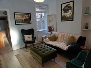 A living room with a green armchair, a sofa, a coffee table, and a bookshelf. - Stylishly Restored House in Oulton Village, between The Broads and The North Sea (Lowestoft)