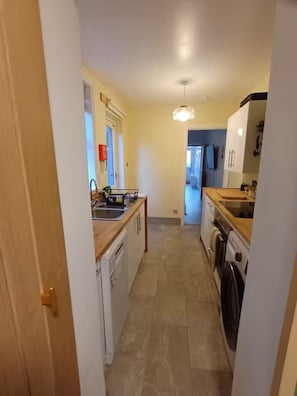 A narrow kitchen with a dishwasher, sink, and a wooden countertop. - Stylishly Restored House in Oulton Village, between The Broads and The North Sea (Lowestoft)