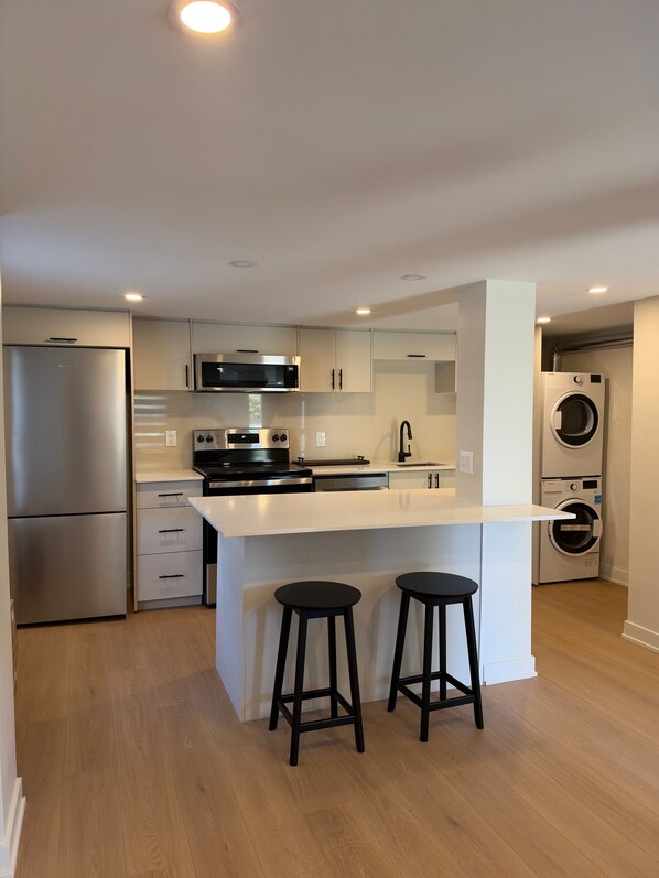 A modern kitchen with stainless steel appliances, a central island with stools, and a built-in washer and dryer.