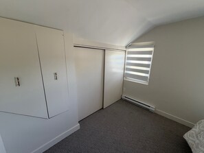A bedroom with a closet, a radiator, and a window with blinds.