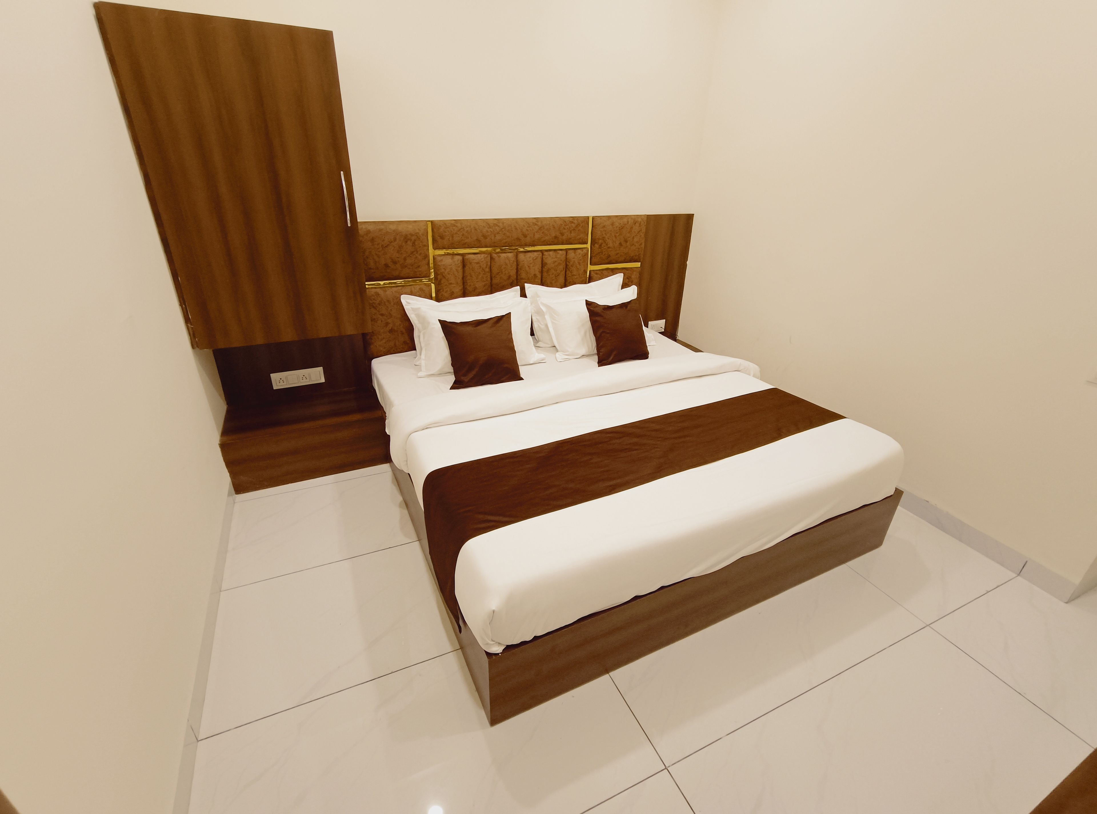Una habitación de hotel con una cama grande, un cabecero de madera y piso con baldosas blancas.