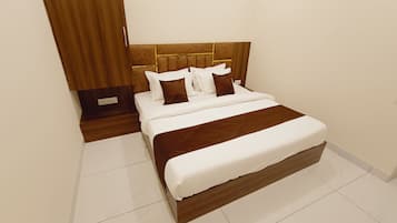Una habitación de hotel con una cama grande, un cabecero de madera y piso con baldosas blancas.