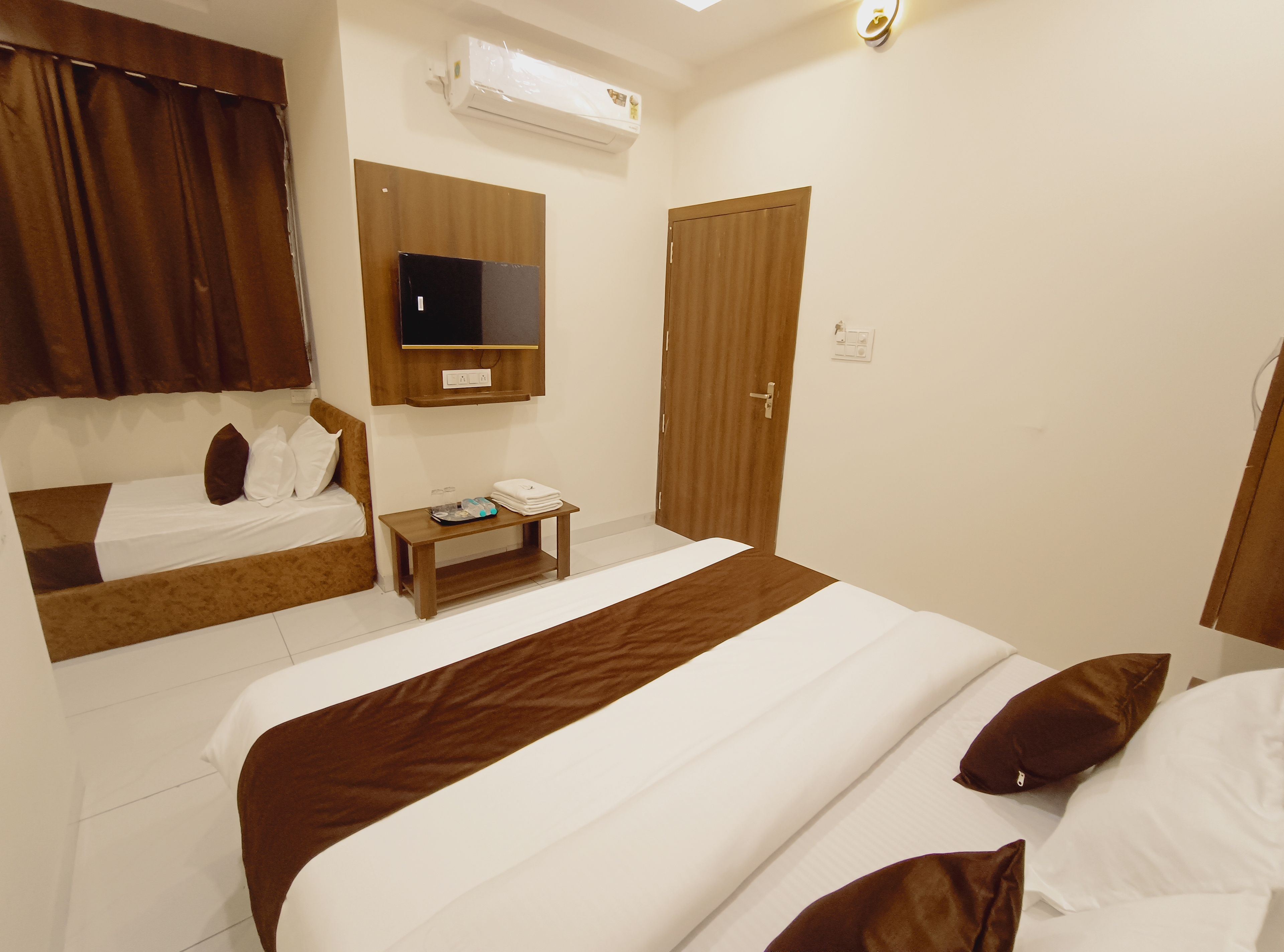 Una habitación de hotel con dos camas, un televisor instalado en la pared, un equipo de aire acondicionado y una puerta de madera.