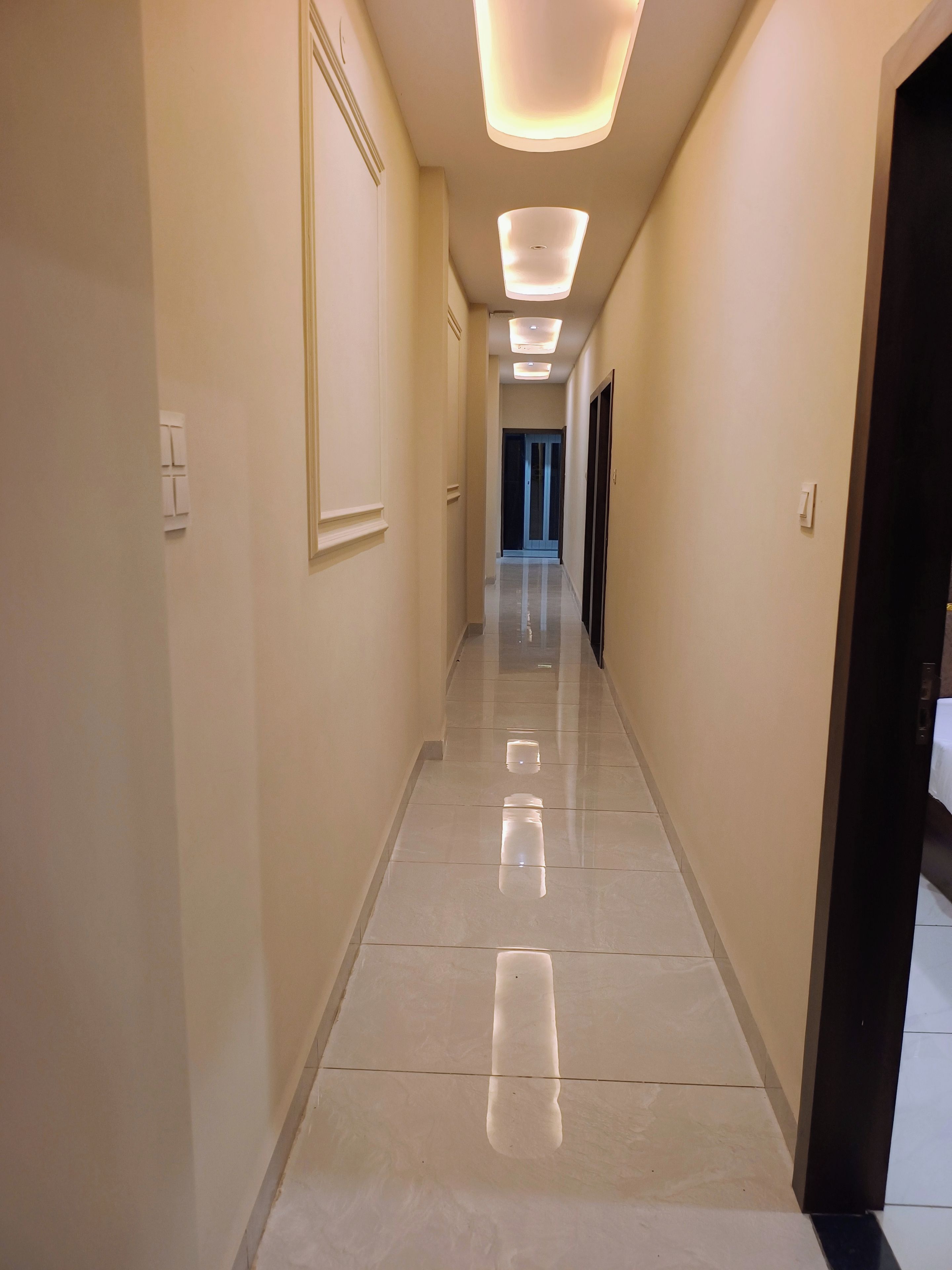 Un pasillo con piso de baldosas reflectantes, iluminación empotrada y puertas que dan a habitaciones.
