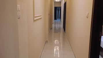 Un pasillo con piso de baldosas reflectantes, iluminación empotrada y puertas que dan a habitaciones.