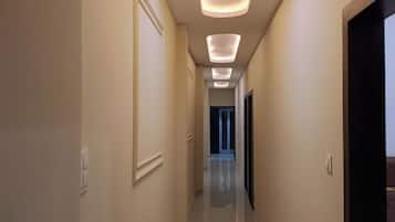 Un pasillo de hotel con diseño moderno, que presenta un largo corredor con varios focos empotrados en el techo y un suelo de baldosas pulidas.